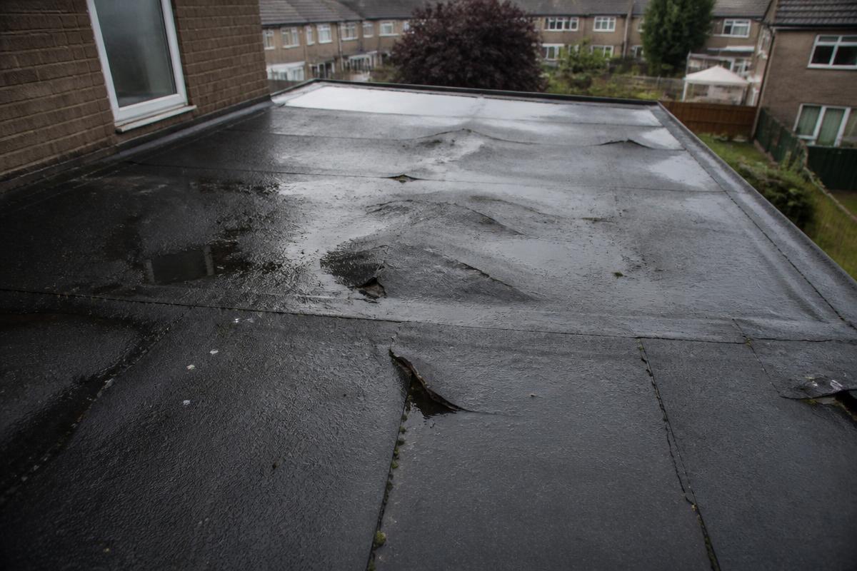 Before flat roof replacement: a UK felt flat roof with blistering, split seams, ponding rainwater and staining in wet weather.