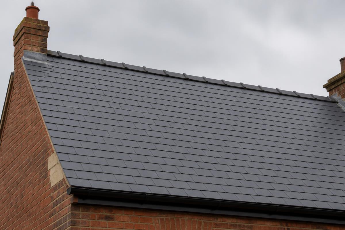 After roof repair: the same British slate roof with replacement slates laid in straight even courses and a sound ridge line.