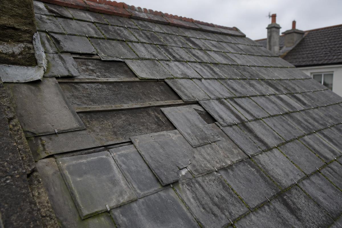 Before roof repair: a UK slate pitched roof with slipped, cracked and patch-repaired slates, exposed battens and moss in the joints.