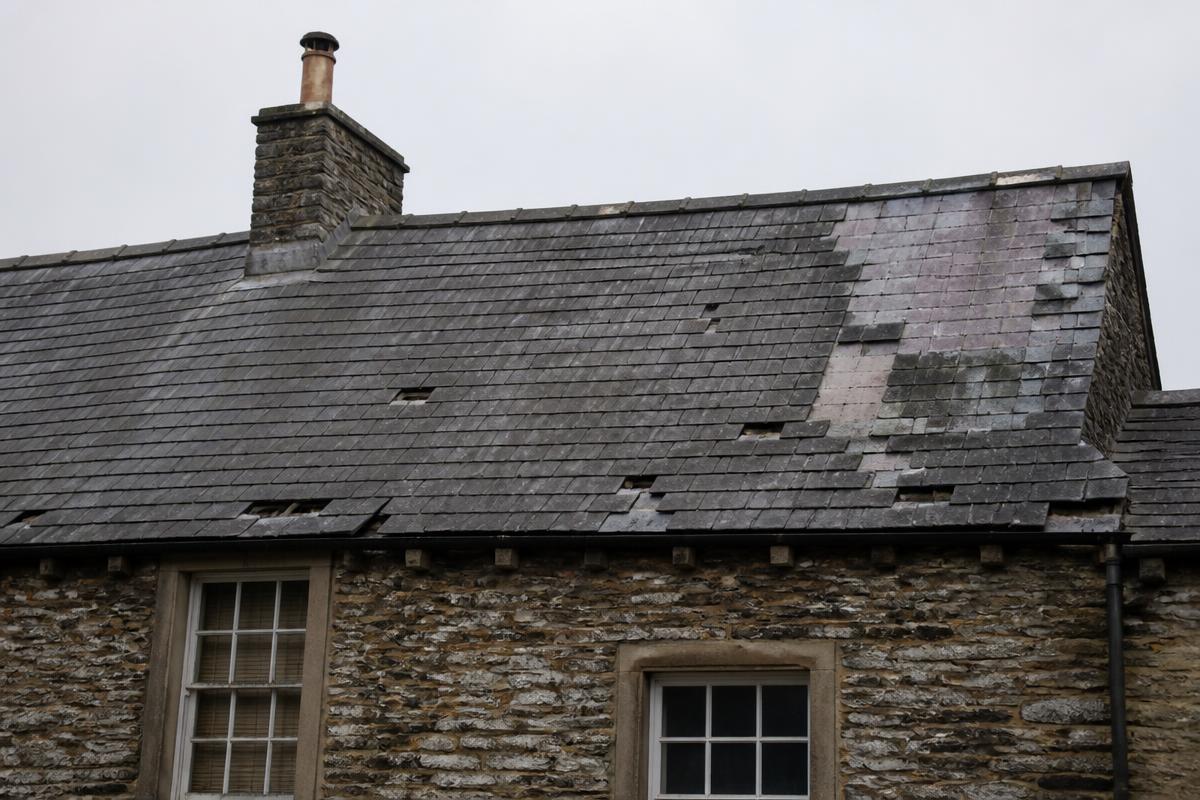 Before re-roofing: a British stone property with a worn slate roof showing missing, delaminating and mismatched patch-repaired slates.