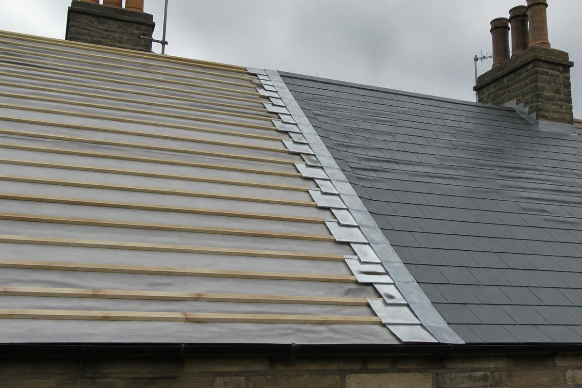 British pitched roof part-way through re-slating, with one side stripped to battens and breathable membrane and the other newly slated with fresh lead flashings.