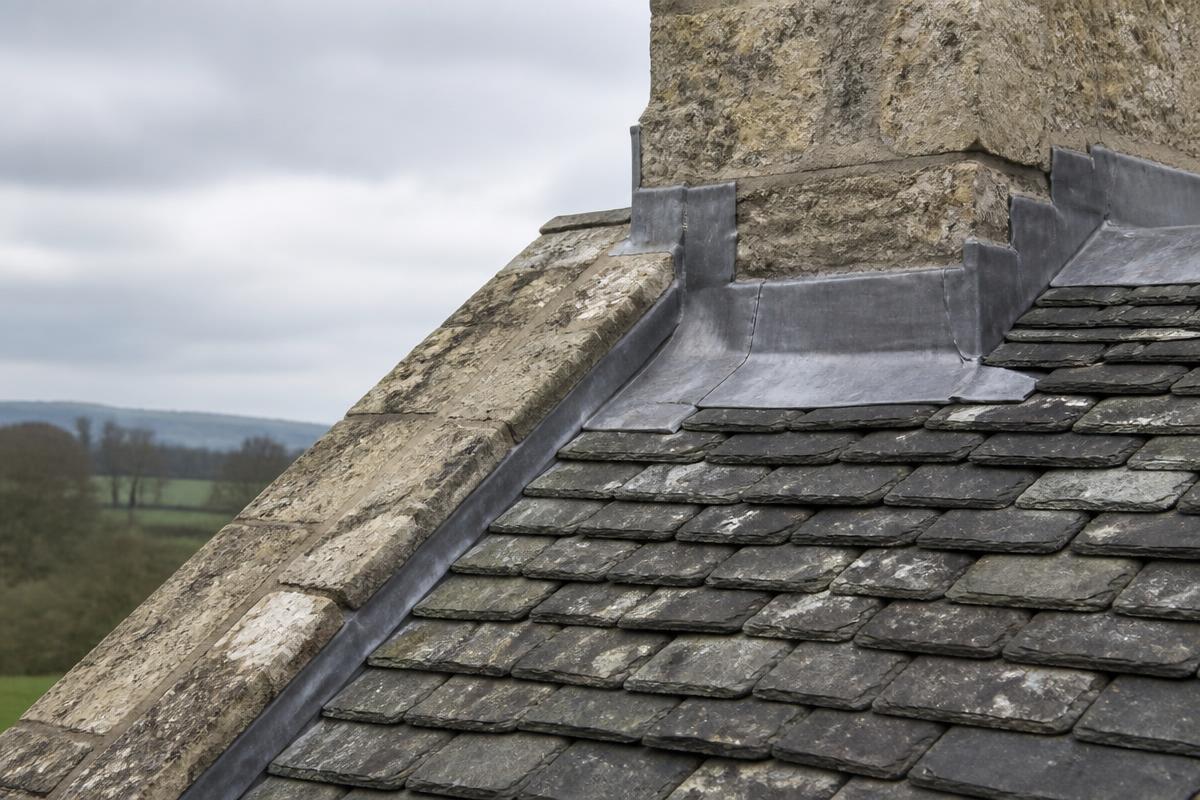 Heritage roofing detail on a traditional British stone building with hand-dressed leadwork and graded reclaimed slates in diminishing courses.