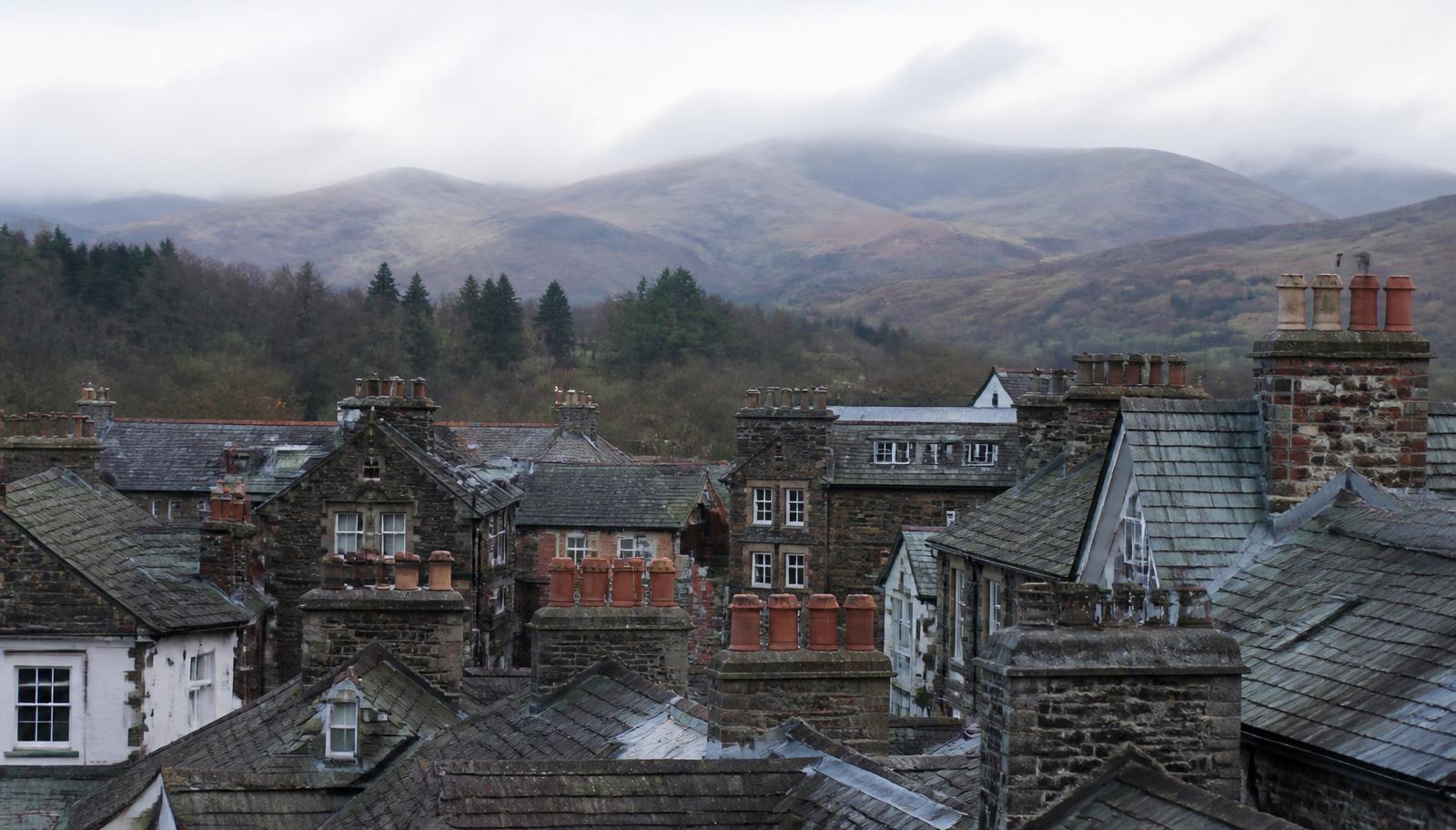 Elevated view over a Cumbrian market town's slate roofs and chimney stacks with the Lake District fells in low cloud.