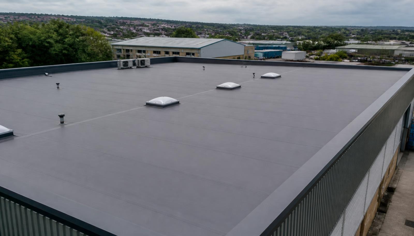 Elevated view of a UK commercial building with a large grey single-ply membrane flat roof, rooflights and steel edge trims.