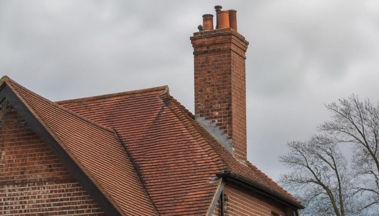 English red clay tile roof on a period brick property with a tall brick chimney, terracotta pots and lead stepped flashing.